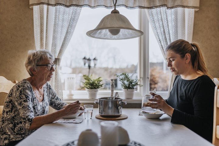 Äldre kvinna och yngre kvinna äter vid matbord
