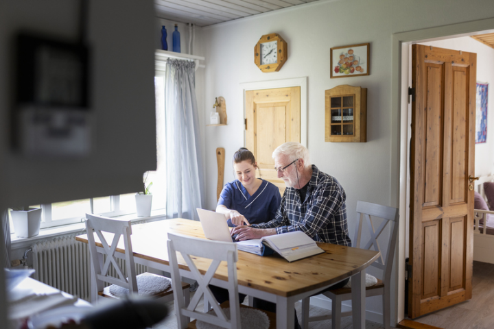 Hemtjänstpersonal som hjälper äldre man med datorn