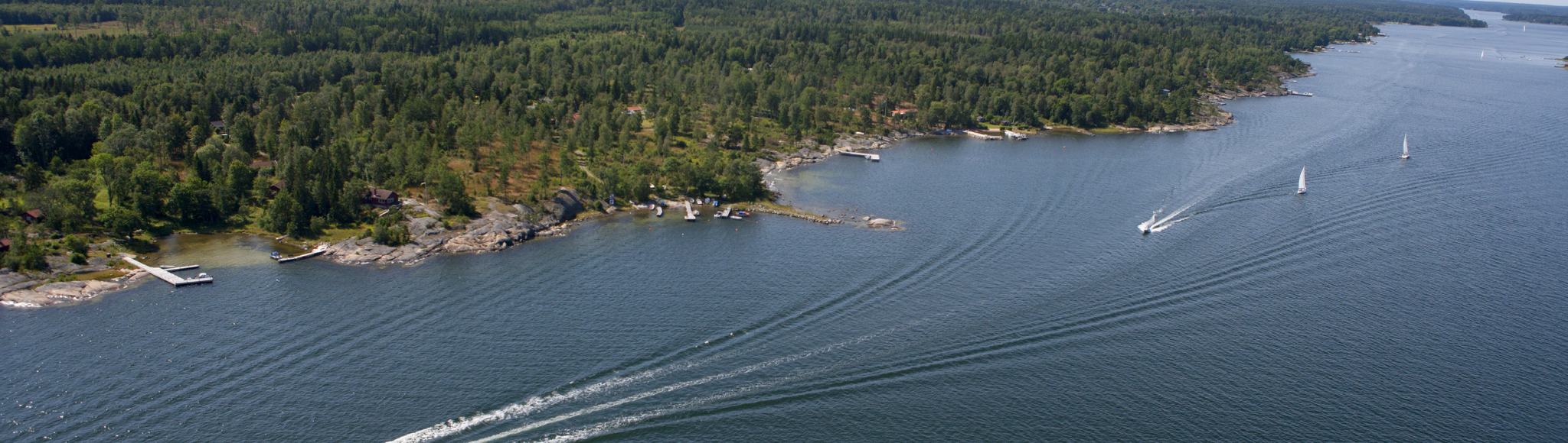 Båtar som seglar längs en klippig och skogbeklädd kust