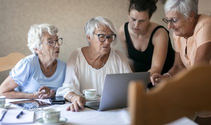 Ung kvinna hjälper tre äldre kvinnor som sitter vid dator