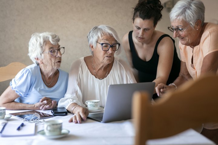 Ung kvinna hjälper tre äldre kvinnor som sitter vid dator