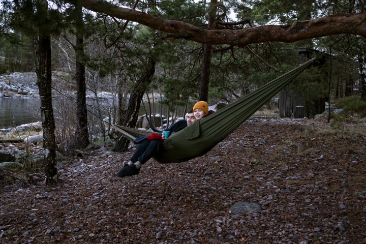 Leende ung man med barn, som fikar i hängmatta i skogen, vid vattnet