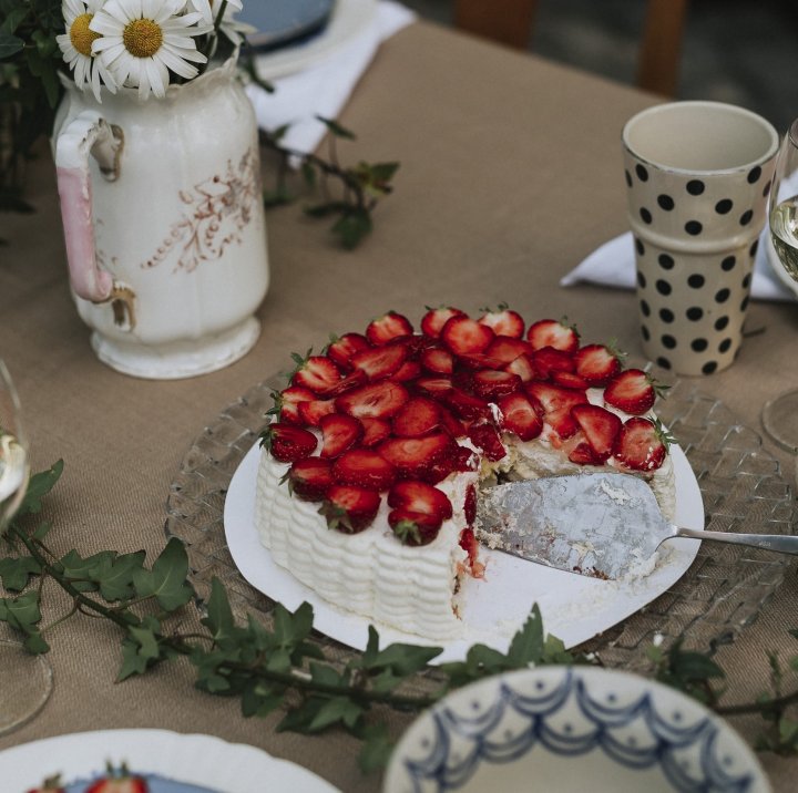 jordgubbstårta på ett bord med blommor och kaffemuggar