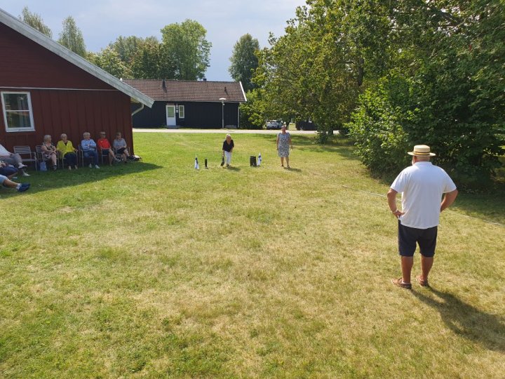 Människor tävlar i stövelkastning på gräsmattan under Seniorkollo på Marholmen.