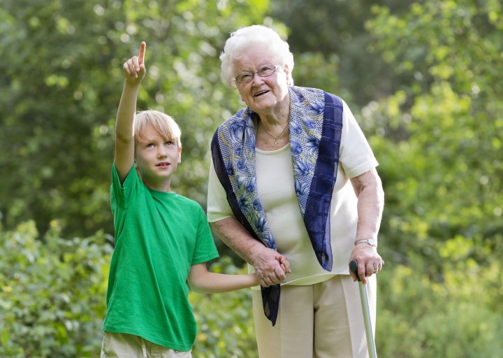 Äldre dam med käpp och pojke ute på promenad och håller varandra i handen