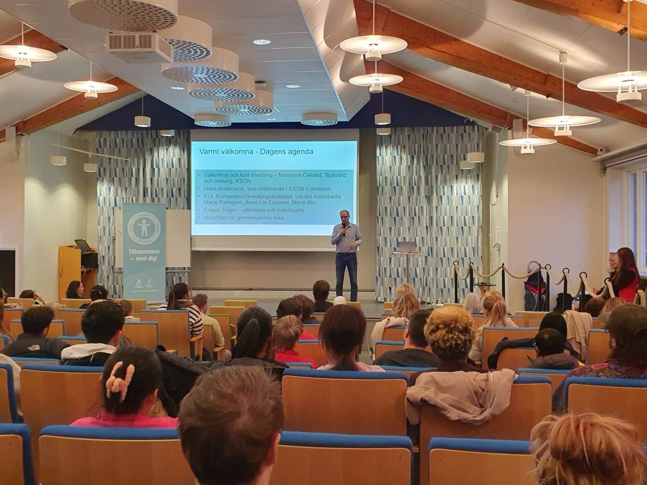 Människor i sal som får information av talare om en utbildning.