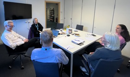 Fem personer sitter kring ett konferensbord