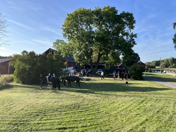Människor i olika åldrar står nära hästar på en hästgård.