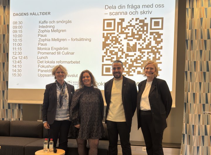 Deltagare på konferens står framför en skärm med dagens punkter framme på en scen.